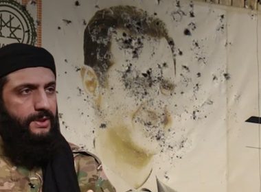 HTŞ lideri Colani ve arkasında Beşşar Esad'ın resminin bulunduğu zarar görmüş bir duvar.